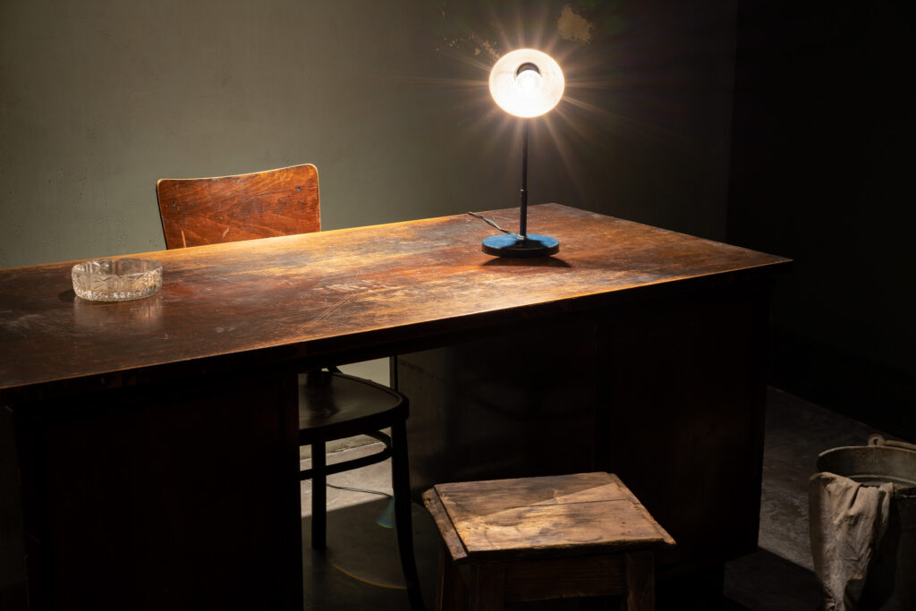 Zdjęcie przedstawia eksponat biurka z krzeslem w pokoju przesłuchań.