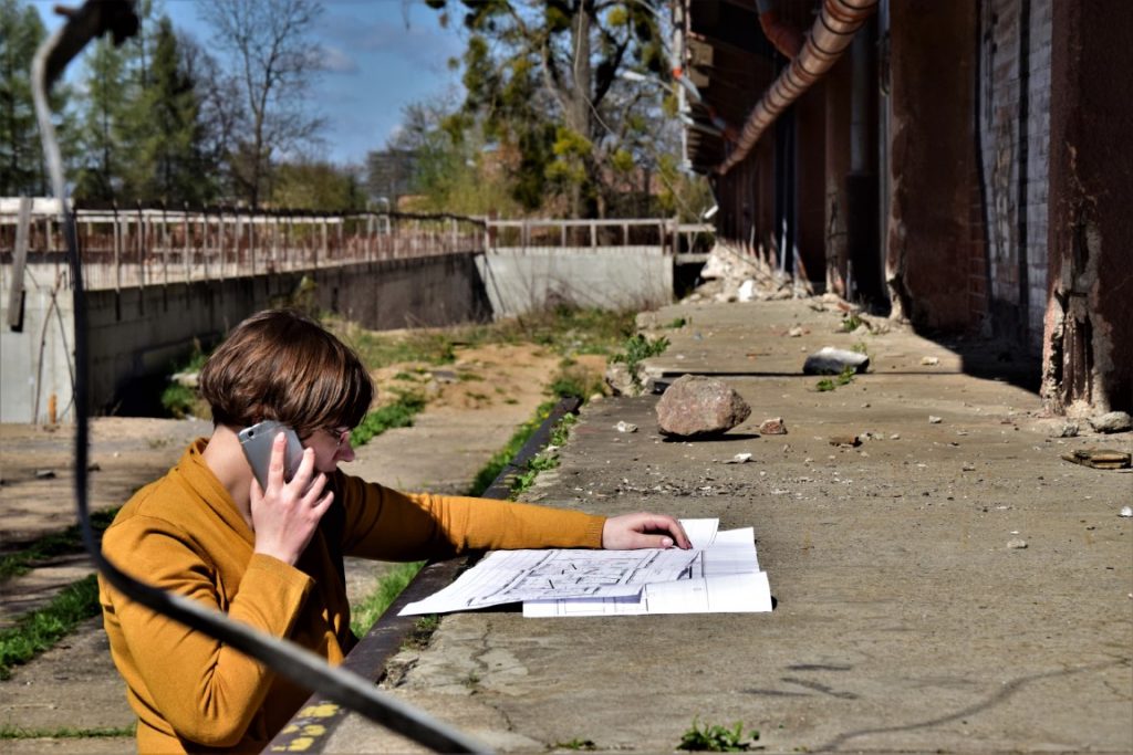 Zdjęcie przedstawia osobę rozmawiającą przez telefon i przeglądającą plan budynku.