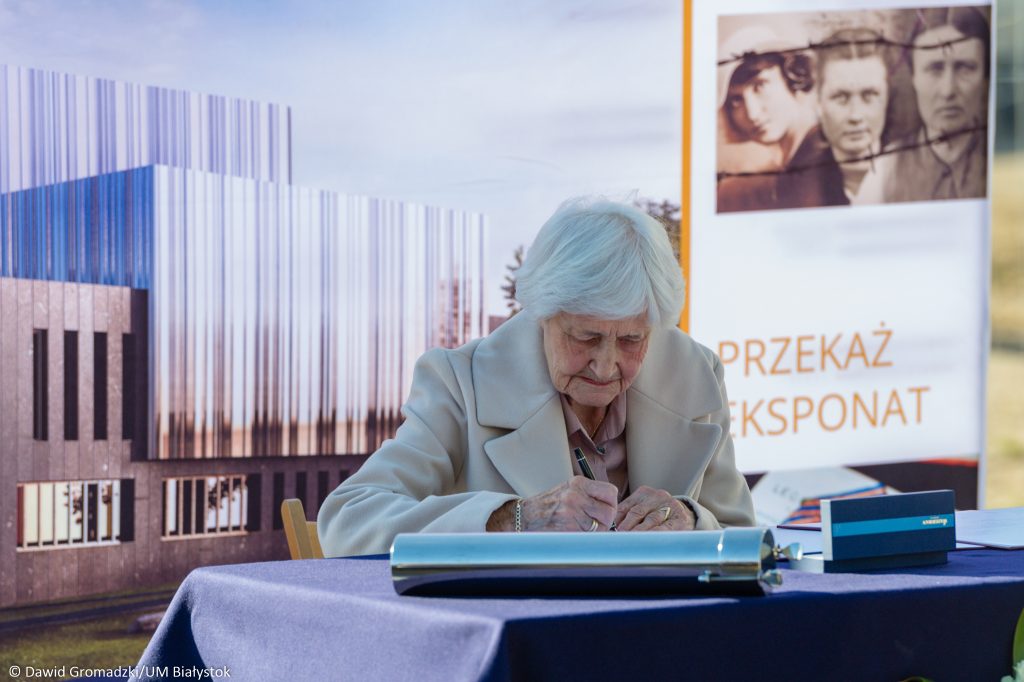 Zdjęcie przedstawia starszą Panią podpisującą dokument.