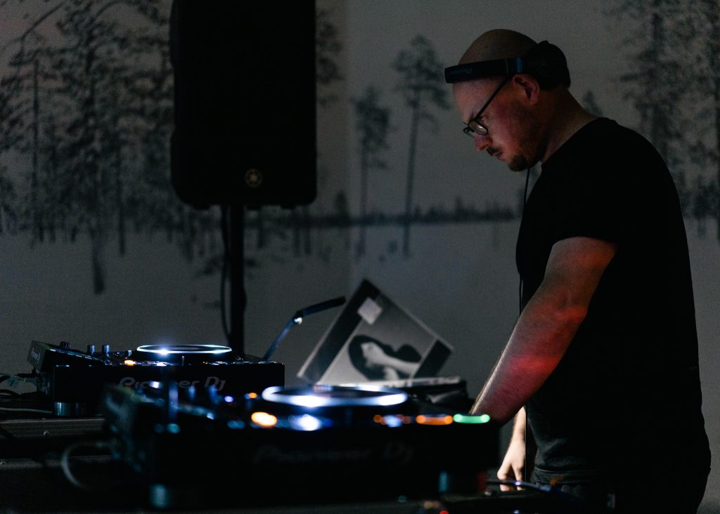 Boczny rzut na DJ'a Jędrzeja Dondziły. Odtwarza stworzoną przez siebie muzykę podczas Pierwszego Syberyjskiego Salonu Ambientu.