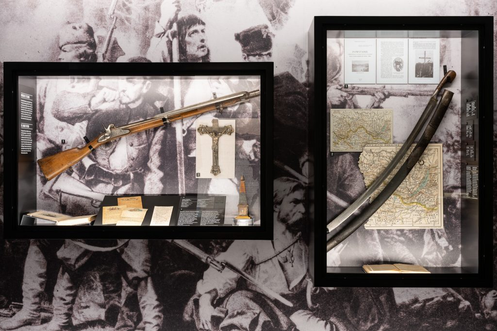 Zdjęcie przedstawia fragment wystawy stałej Muzeum Pamięci Sybiru, na której widać strzelbę oraz szablę
