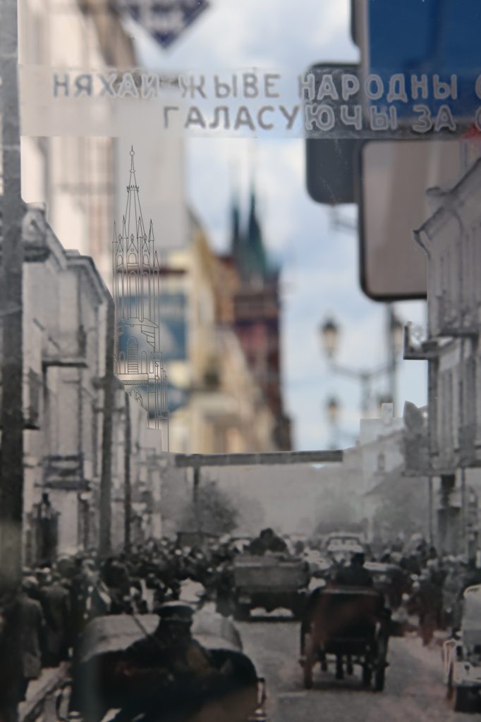 Jeden z pięciu elementów wystawy plenerowej "Przeszłość oczami teraźniejszości. Białystok' 39". W ramie przezroczysta tafla z nadrukowanym archiwalnym, czarno-białym zdjęciem. Przez niezadrukowany fragment tafli przebija widok ulicy. Współczesny widok uzupełnia archiwalną fotografię.