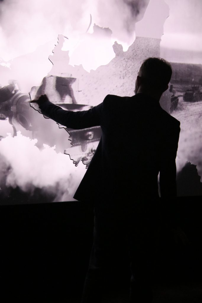Ciemna sylwetka mężczyzny na tle projekcji czarno-białego filmu na wystawie stałej Muzeum Pamięci Sybiru.