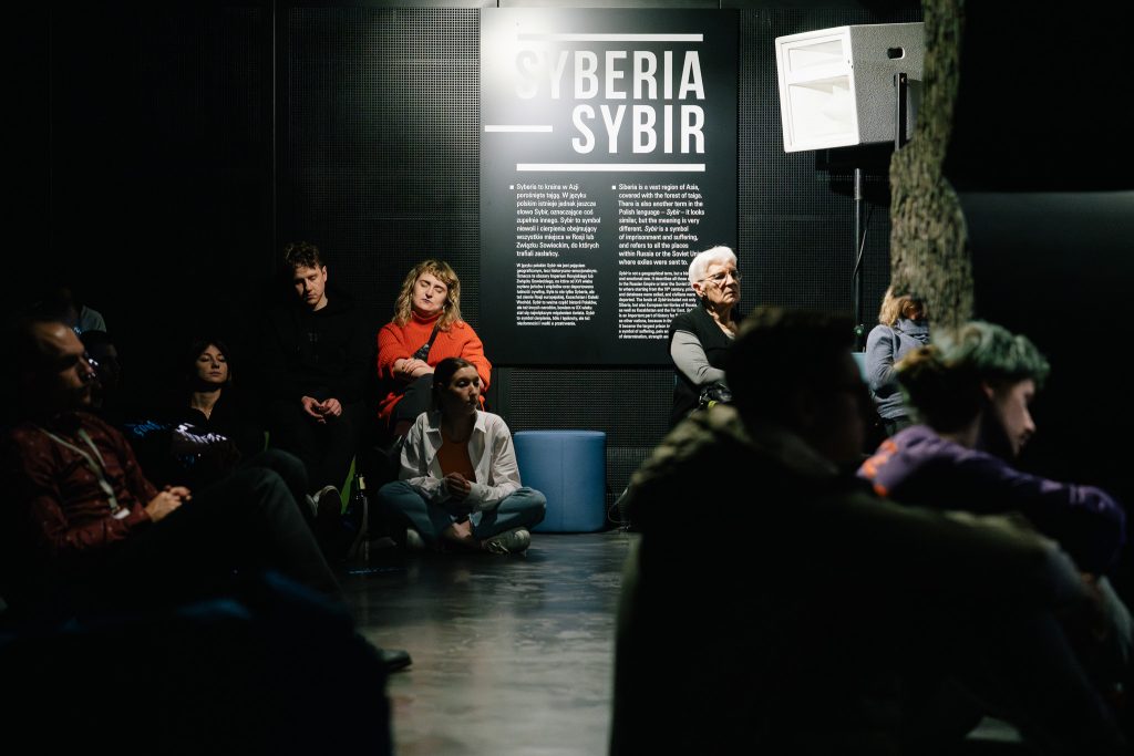 Zasłuchani uczestnicy siedzą na wystawie stałej Muzeum Pamięci Sybiru podczas Drugiego Syberyjskiego Salonu Ambientu