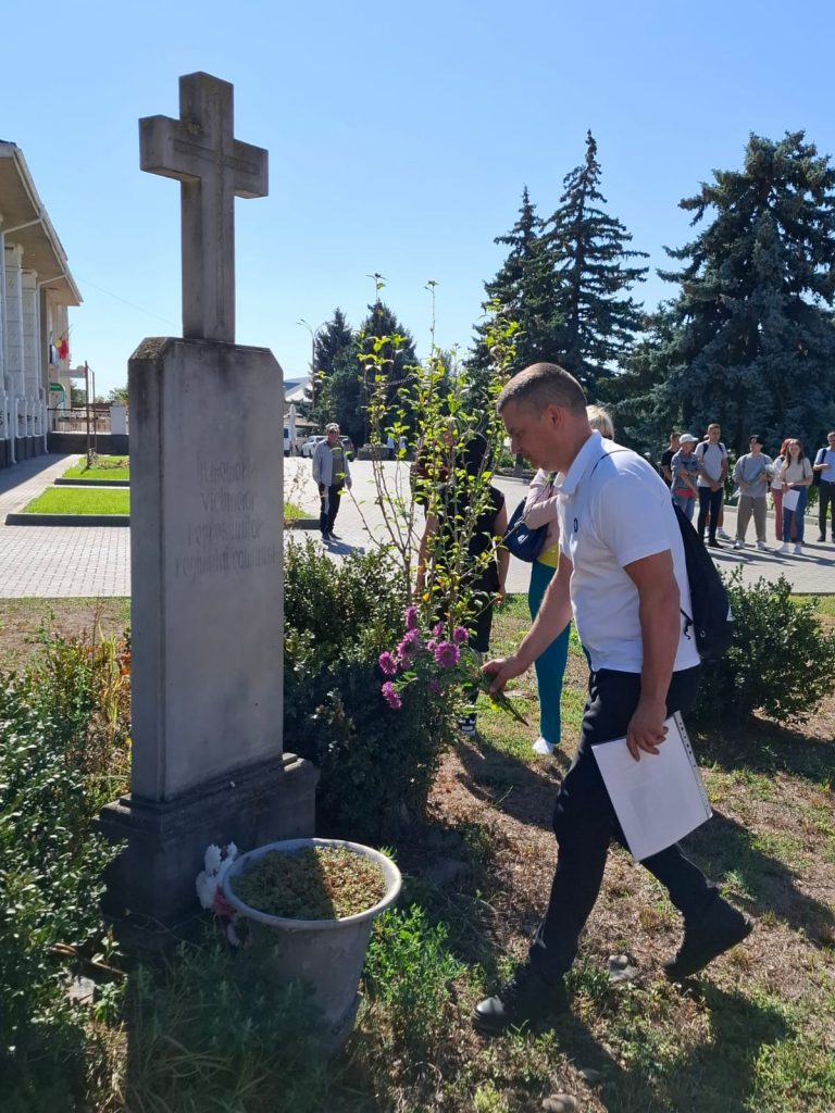 Mężczyzna w białej koszulce składa kwiaty pod pomnikiem.