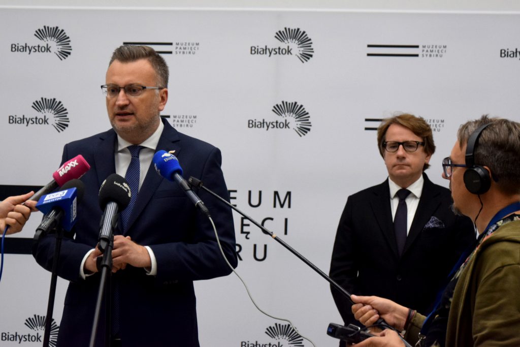 Zastępca prezydenta miasta Rafał Rudnicki przemawia do mikrofonu podczas konferencji prasowej. Z tyłu stoi Dyrektor Muzeum Pamięci Sybiru prof. Wojciech Śleszyński.