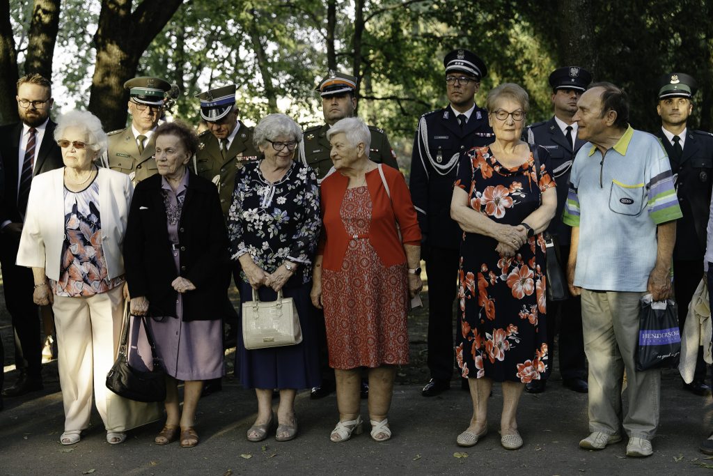 Grupa Sybiraczek stojąc uśmiechają się i rozmawiają. Za nimi stoją przedstawiciele służb mundurowych.
