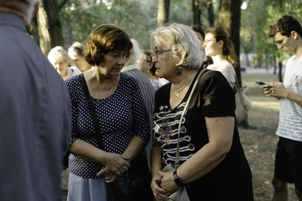 Dwie kobiety rozmawiają ze sobą. W tle grupa osób.