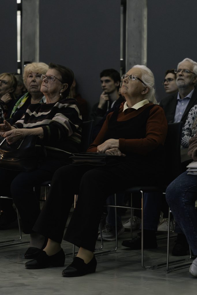 Grupa uczestników spotkania z zainteresowaniem patrzy przed siebie i słucha wykładu.