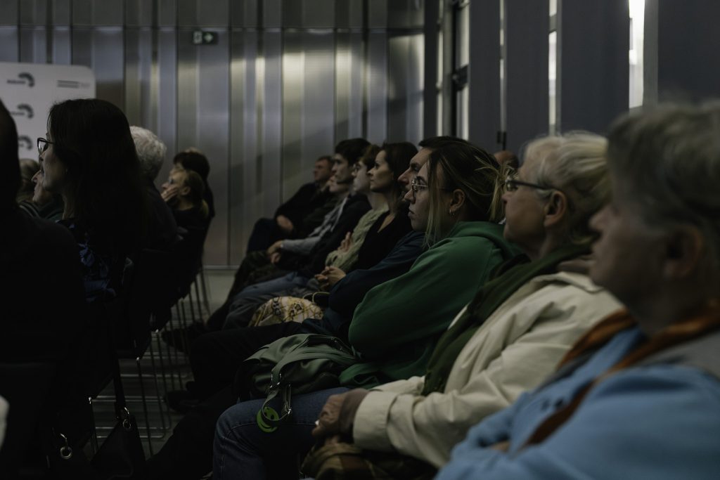 Grupa uczestników spotkania z zainteresowaniem patrzy przed siebie i słucha wykładu.