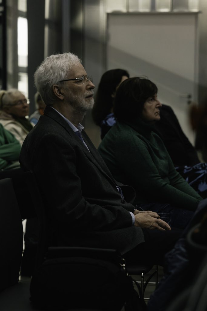 Grupa osób słucha wykładu. Na pierwszym planie starszy mężczyzna.