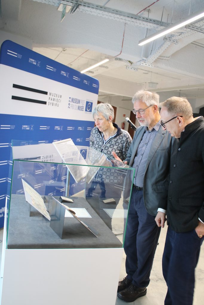 Dwóch mężczyzn oraz kobieta stoją i przyglądają się eksponatom w szklanej gablocie.