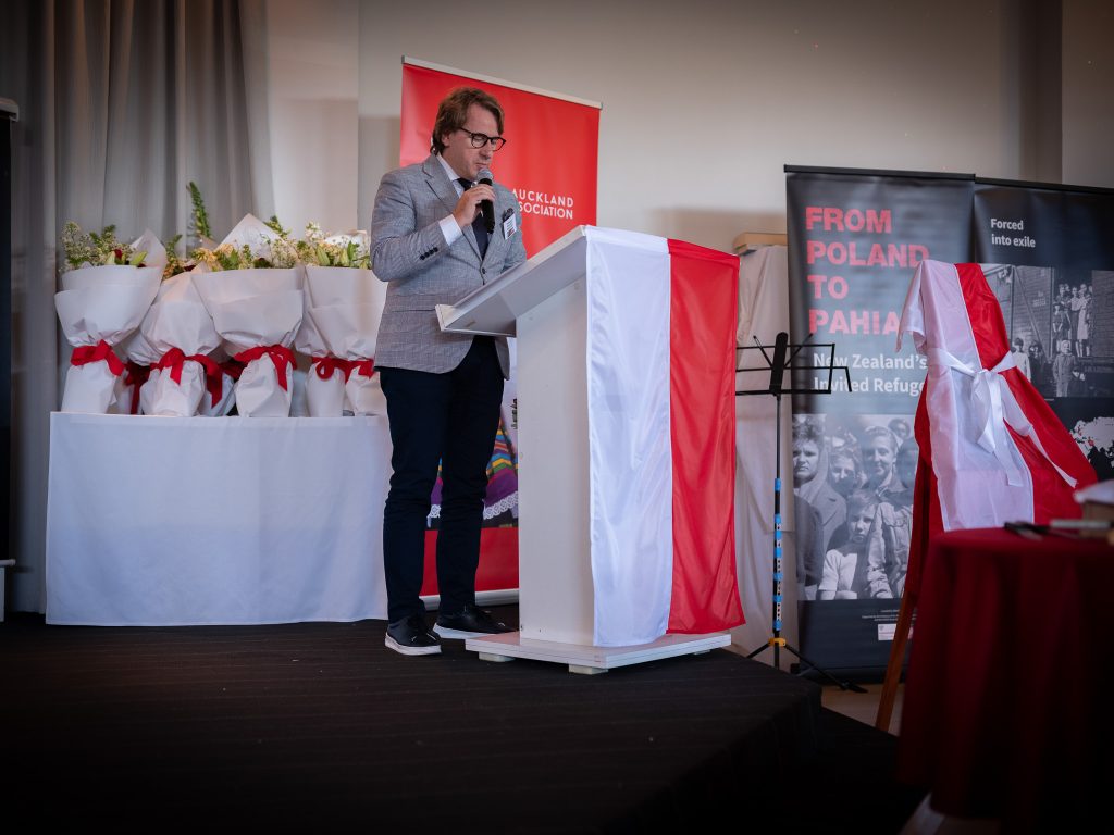 Prof. Wojciech Śleszyński, dyrektor Muzeum Pamięci Sybiru podczas przemówienia. Stoi za mównica udekorowaną biało-czerwoną flagą.