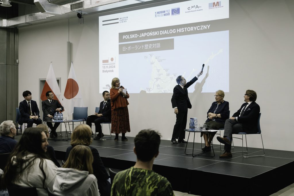 Prezes Matsumoto Yuzo pokazuje na mapie wspominane wyspy. W ręku trzyma mikrofon. Obok niego stoi tłumaczka.