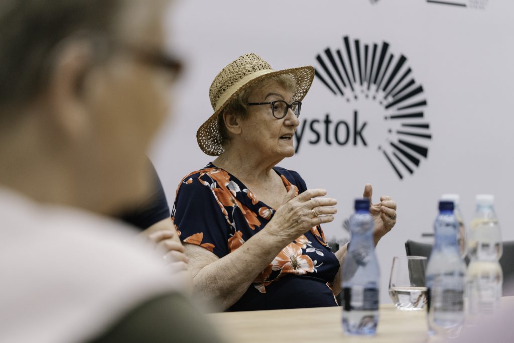 Sybiraczka, Pani Teresa Borkowska przemawia przy stole. W tle widoczne jest logo miasta Białegostoku.