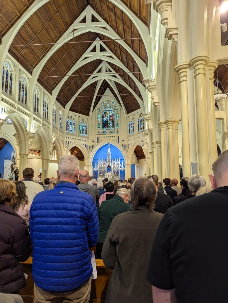 Wierni uczestniczą w mszy świętej. Kilkadziesiąt osób stoi przodem do ołtarza.