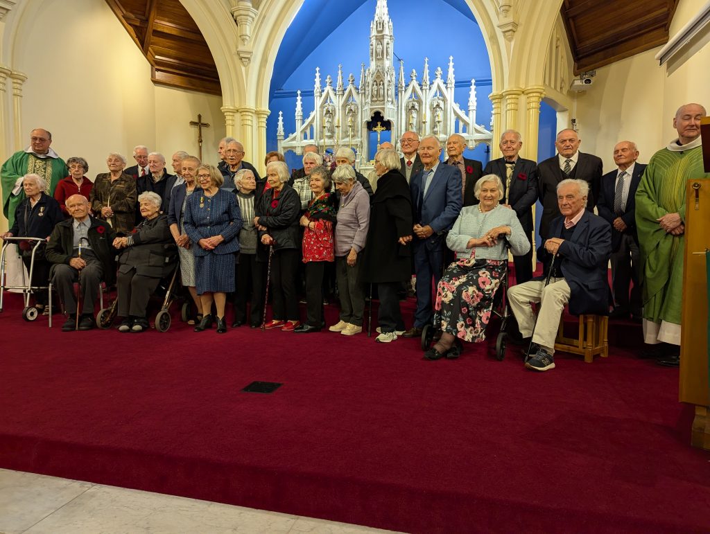 Grupa starszych osób na tle ołtarza. Po obu stronach stoją duchowni.
