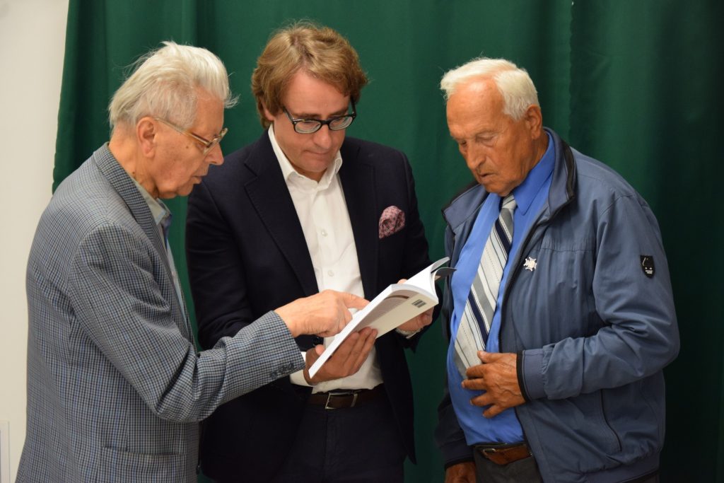 Trzech mężczyzn stoi i przygląda się otwartej książce. Po lewej jest to autor książki, Marian Stecyk, w środku stoi prof. Wojciech Śleszyński, dyrektor Muzeum Pamięci Sybiru.