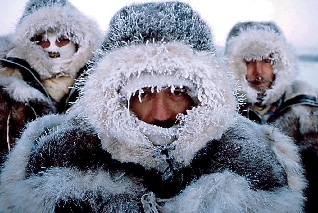 Trzech mężczyzn w tradycyjnych ciepłych, futrzanych ubiorach. Szron pokrywający futrzane kaptury sugeruje obecność bardzo silnego mrozu.