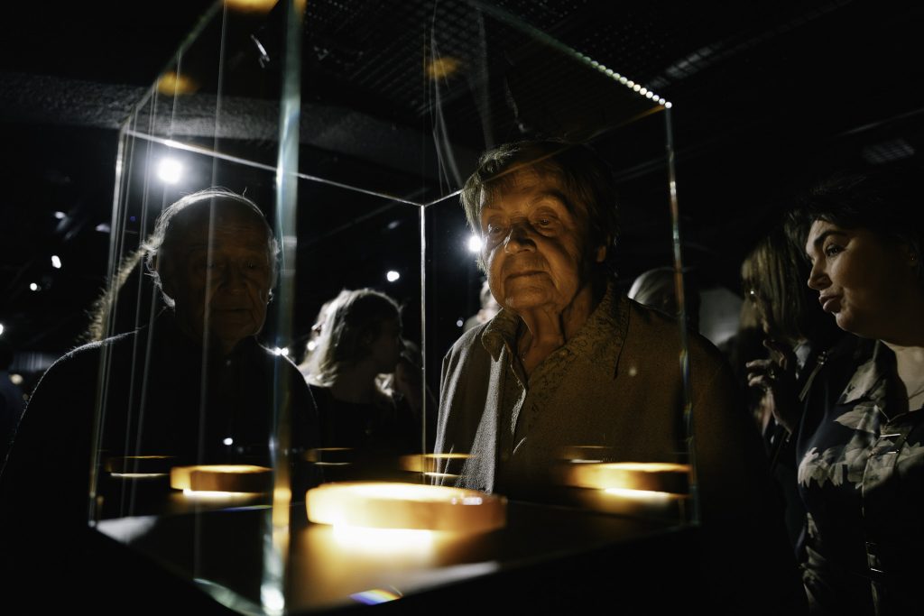 Dwoje starszych osób ogląda jeden z eksponatów. W tle jest widocznych kilku innych zwiedzających.