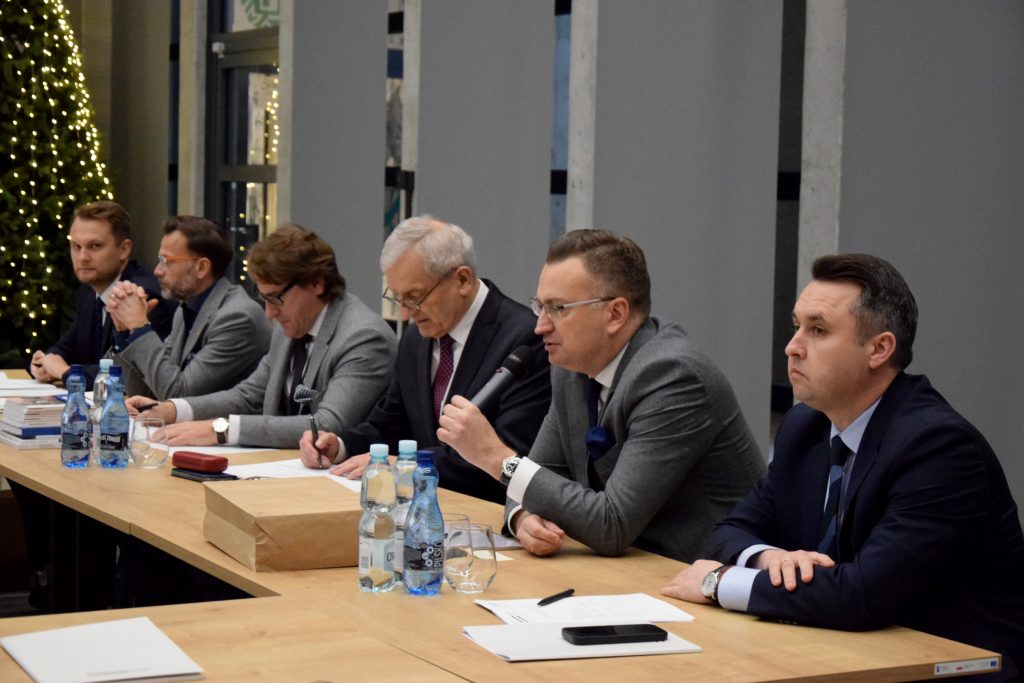 Rafał Rudnicki, zastępca prezydenta Białegostoku przemawia do mikrofonu siedząc przy stole. Obok inni uczestnicy spotkania.