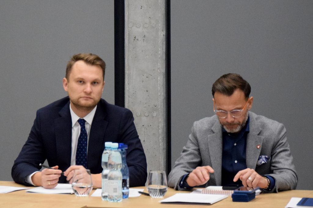 Przy stole siedzą Krzysztof Truskolaski, poseł na Sejm oraz Jacek Brzozowski, wojewoda podlaski. Na stole znajdują się notatki, butelki wody i szklanki.