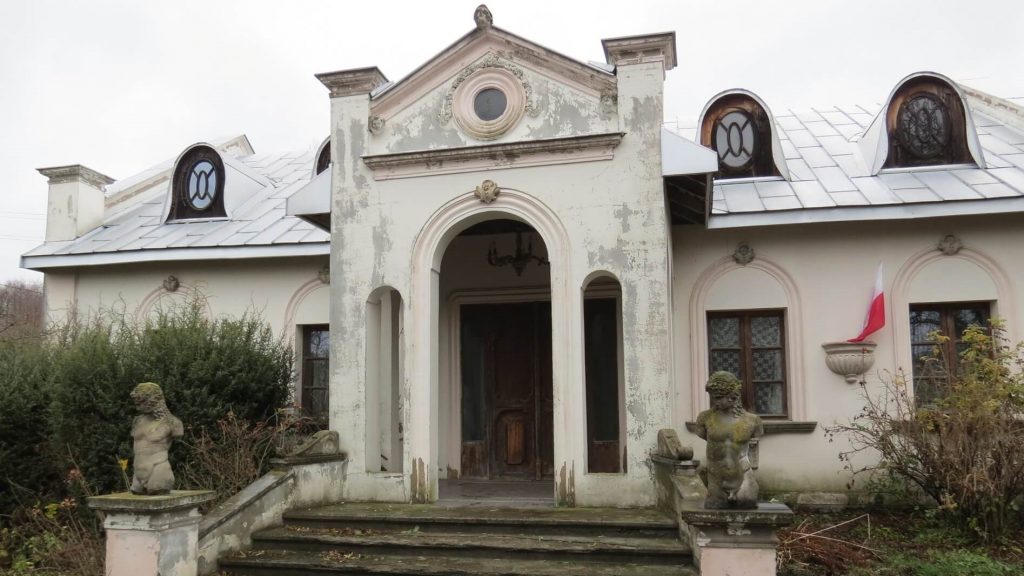 Stary, murowany dom, wyglądający na opuszczony, Na domu zawieszona jest polska flaga.