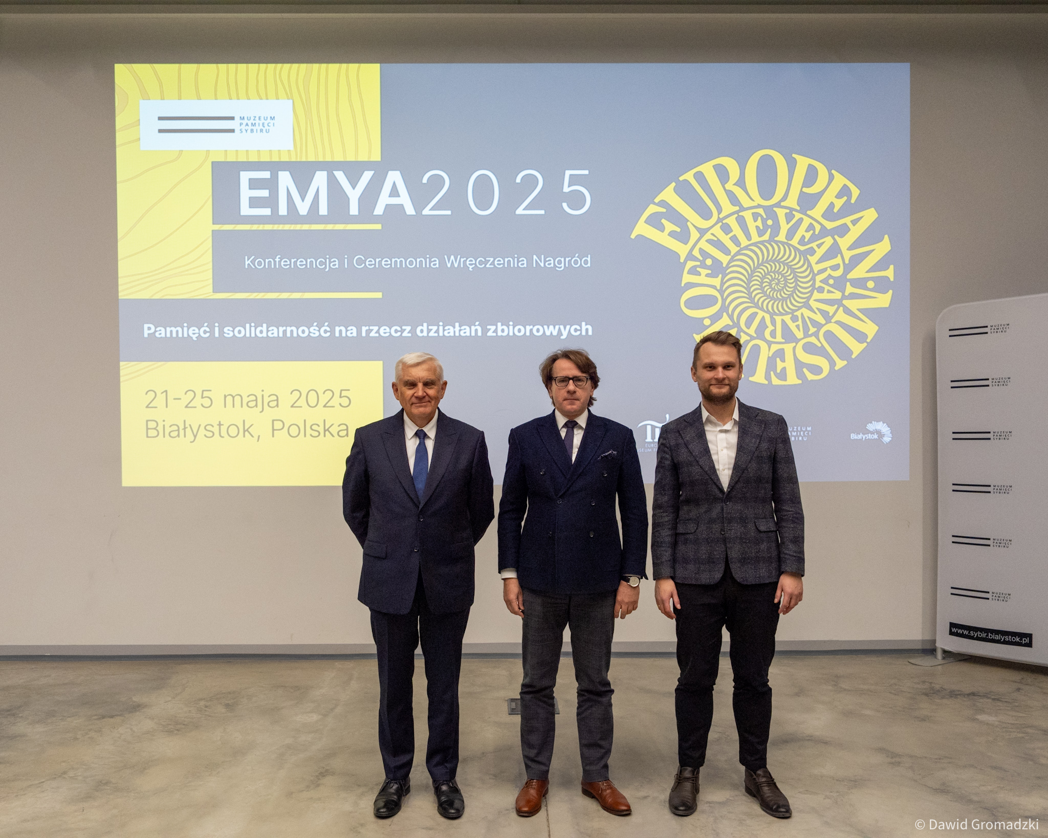 Od lewej Tadeusz truskolaski, prezydent Białegostoku, prof. Wojciech Śleszyński, dyrektor Muzeum Pamięci Sybiru oraz Krzysztof Truskolaski, poseł na Sejm. Stoją na tle slajdu z informacją o EMYA2025.
