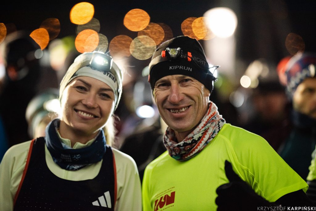 Kobieta i mężczyzna w strojach sportowych. Mają czołówki i czapki, uśmiechają się.