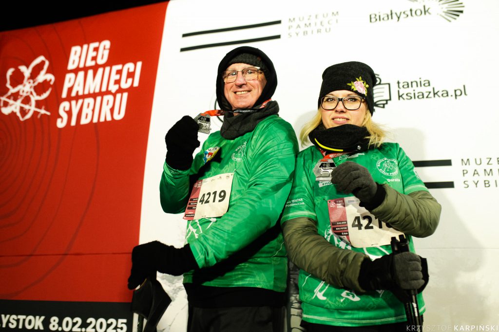 Kobieta i mężczyzna, uczestnicy biegu, ubrani są w zielone bluzy. Pozują uśmiechnięci trzymając w ręku medale.