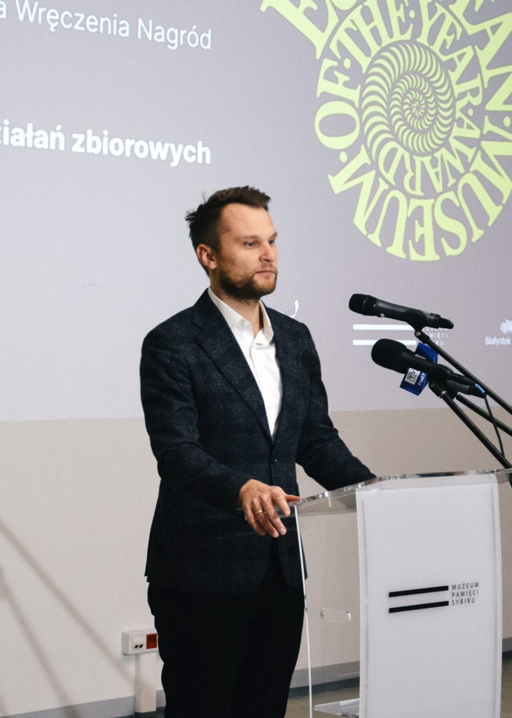 Poseł na Sejm RP Krzysztof Truskolaski  przy mikrofonie podczas przemówienia. W tle widoczne logo EMYA.