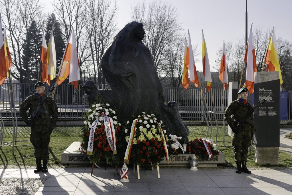 Pomnik poświęcony Bohaterskim Matkom Sybiraczkom. Obok stoi dwóch żołnierzy, pod pomnikiem są wieńce. Z tyłu znajdują się flagi.