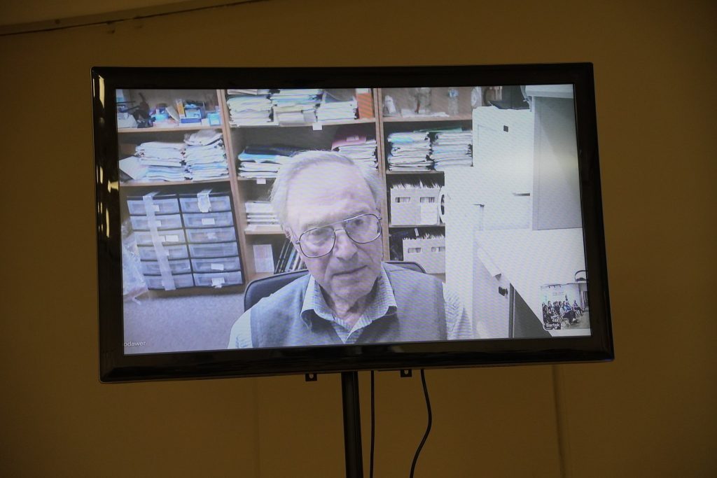 Na ekranie telewizora widać prof. Alexandra Włodawera podczas wideokonferencji z uczestnikami spotkania.