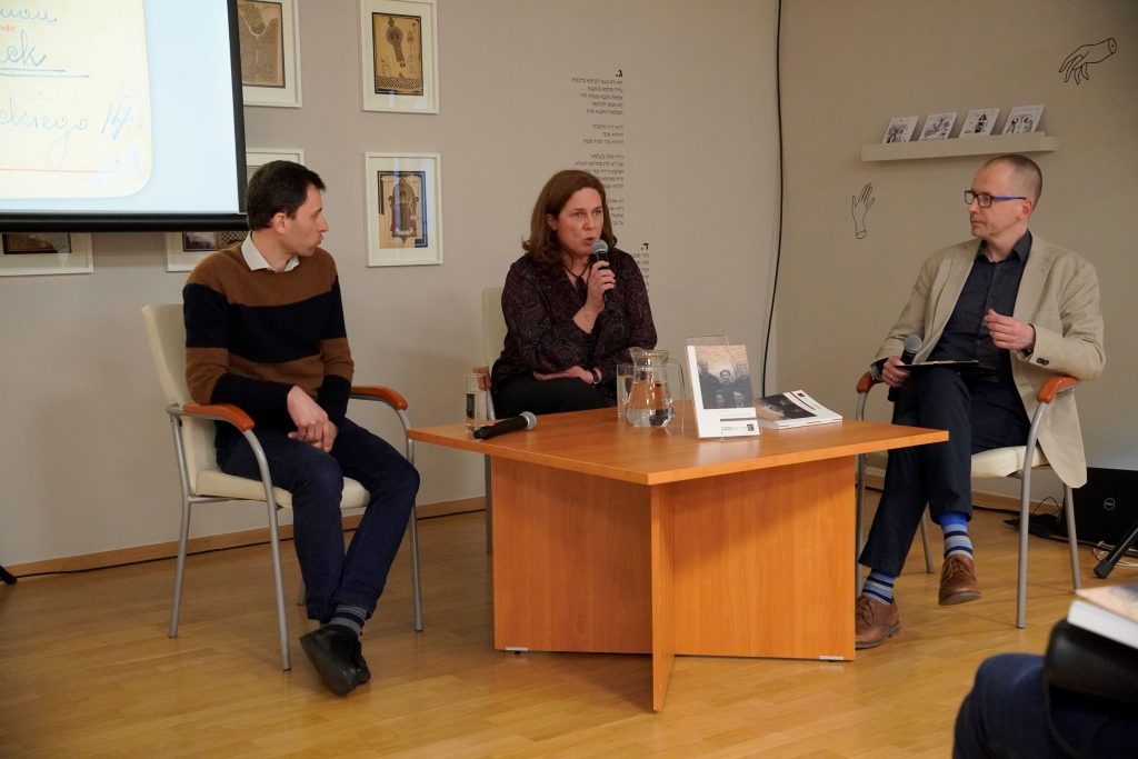 Przy stoliku siedzą: dr Przemysław Kaniecki z Muzeum „Polin”, Anna Pyżewska z Działu Naukowego – Instytutu im. Seweryna Nowakowskiego Muzeum Pamięci Sybiru, dr Marcin Zwolski, kierownik działu naukowego Muzeum Pamięci Sybiru. P. Anna przemawia do zgromadzonych osób. Na stoliku stoi książka "Tam, gdzie kończył się świat".