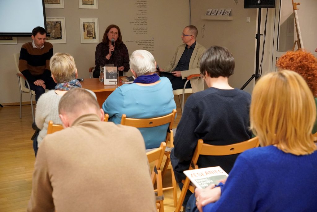 Przy stoliku siedzą: dr Przemysław Kaniecki z Muzeum „Polin”, Anna Pyżewska z Działu Naukowego – Instytutu im. Seweryna Nowakowskiego Muzeum Pamięci Sybiru, dr Marcin Zwolski, kierownik działu naukowego Muzeum Pamięci Sybiru. P. Anna przemawia do zgromadzonych osób. Na stoliku stoi książka "Tam, gdzie kończył się świat". Widać też kilka osób z publiczności. Wszyscy siedzą.