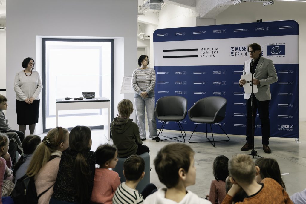 Prof. Wojciech Śleszyński przemawia podczas inauguracji kwietniowego "Eksponatu Miesiąca". Przy gablocie stoją dwie