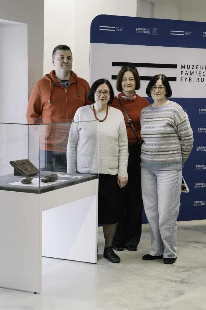 Rodzina potomków Heleny Pałki. Trzy starsze kobiety oraz mężczyzna. Stoją przy szklanej gablocie z eksponatem miesiąca. W tle za nimi widoczne jest logo Muzeum.