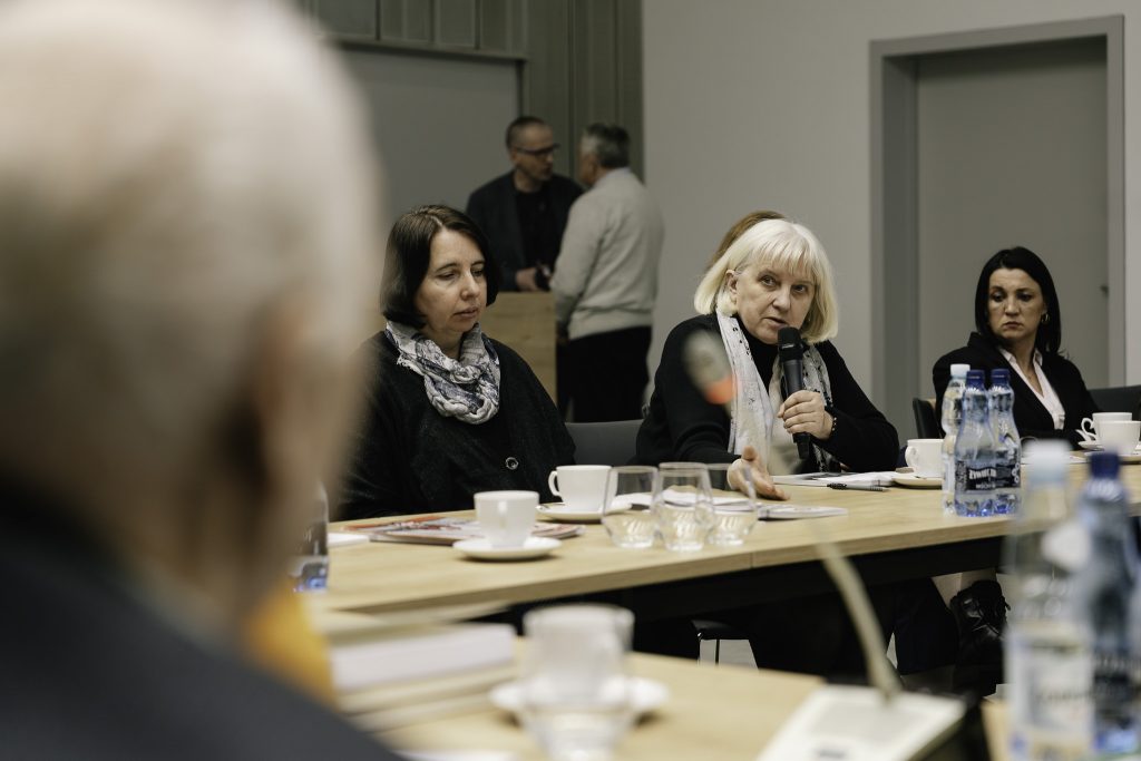 Jedna z uczestniczek wydarzenia przemawia. Trzyma w ręku mikrofon. Obok niej siedzą inne uczestniczki.