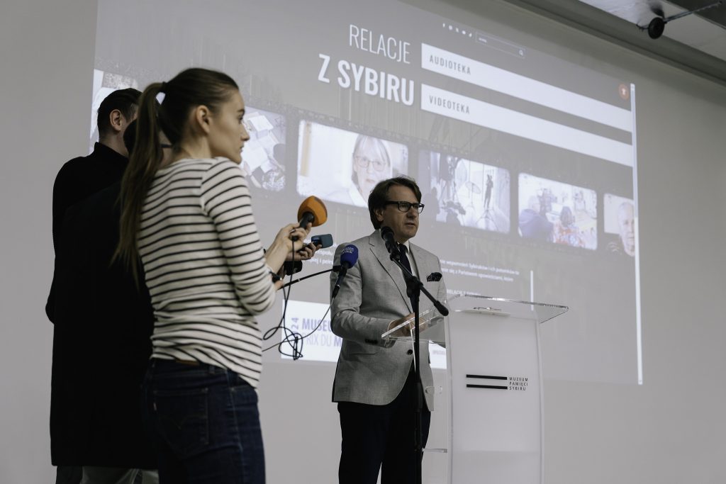 Dyrektor Muzeum Pamięci Sybiru, prof. dr hab. Wojciech Śleszyński przemawia przy mównicy. W tle za nim na ścianie jest wyświetlana nowo powstała strona internetowa poświęcona Relacjom z Sybiru.