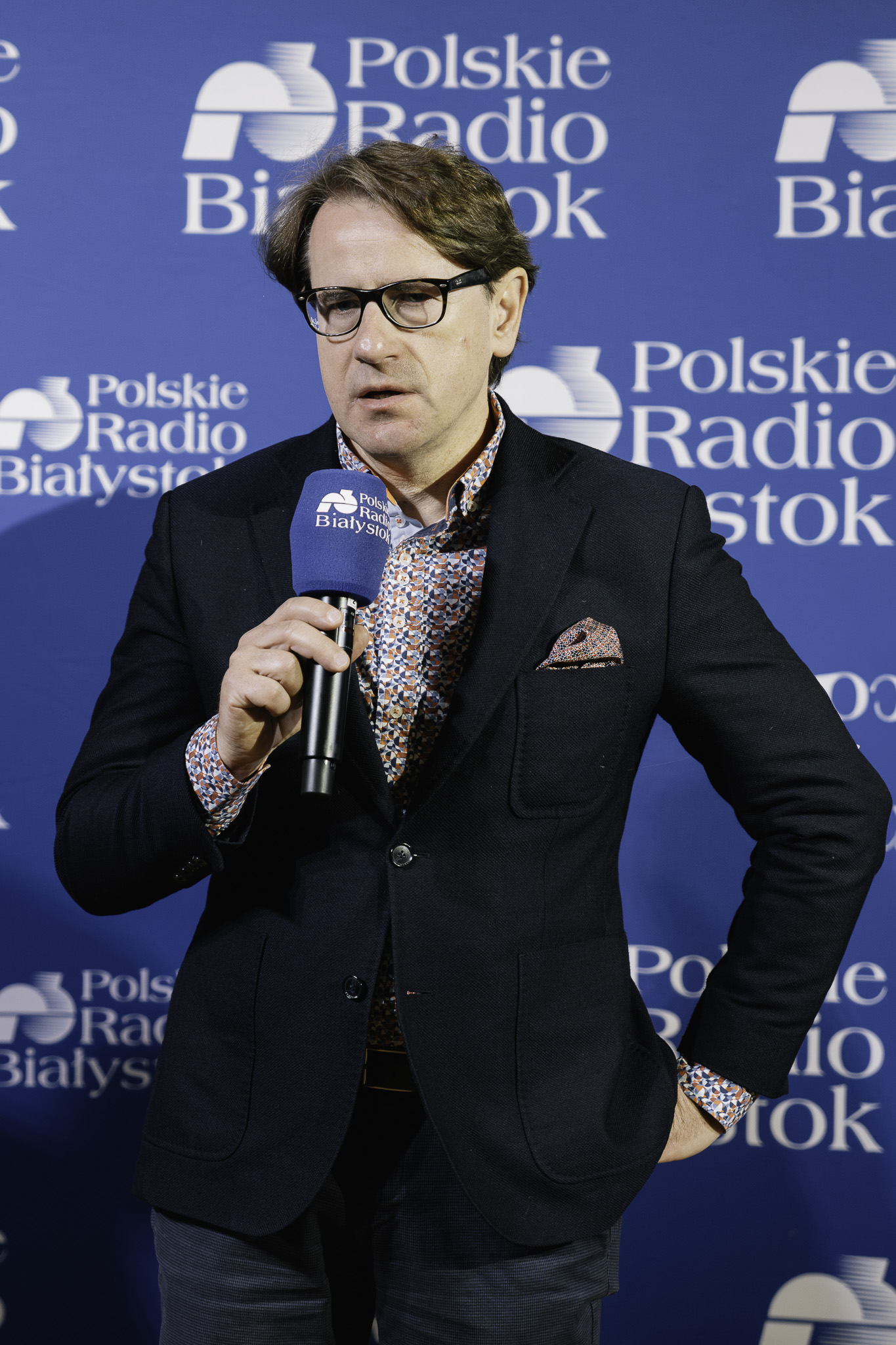 Prof. Wojciech Śleszyński podczas przemówienia na konferencji prasowej. W ręku trzyma mikrofon. Za Nim jest widoczne logo Polskiego Radia Białystok na niebieskim tle.