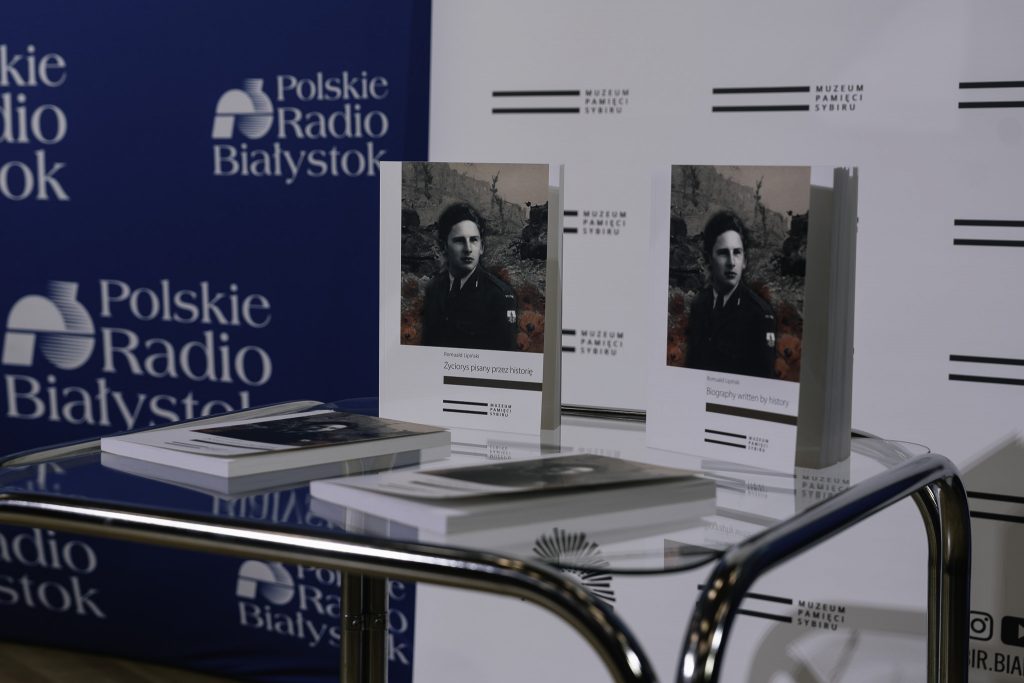 Na stole leżą książki „Życiorys pisany przez historię”. Autorem jest płk. Romuald Lipiński. Okładka książki przedstawia młodego mężczyznę w wojskowym mundurze.