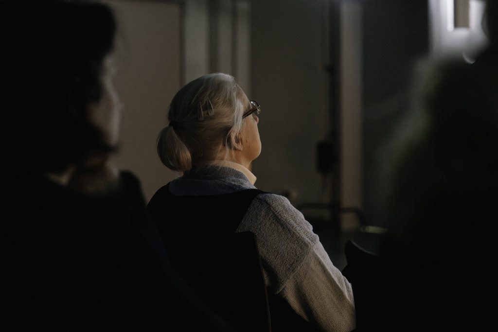 Starsza kobieta z siwymi włosami i w okularach, w wielkim skupieniu ogląda.