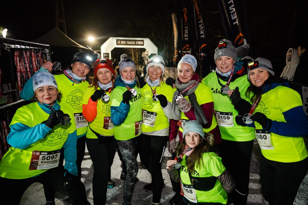 Drużyna kobiet, biegaczek, w jednakowych zielonych koszulkach z napisem Fafarafa, z medalami, na tle mety i napisu Bieg Pamięci Sybiru.